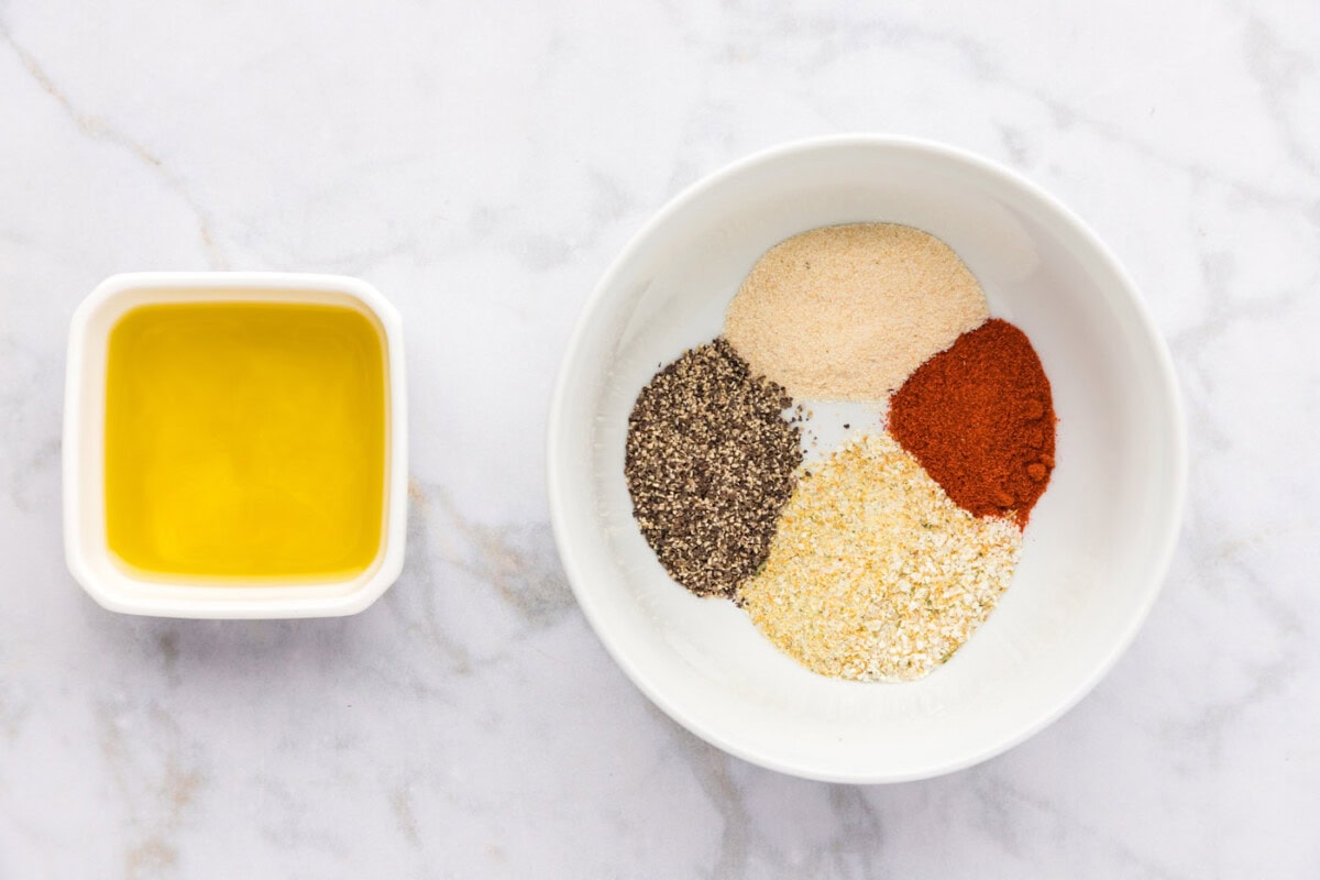 seasonings in a bowl next to a bowl of olive oil