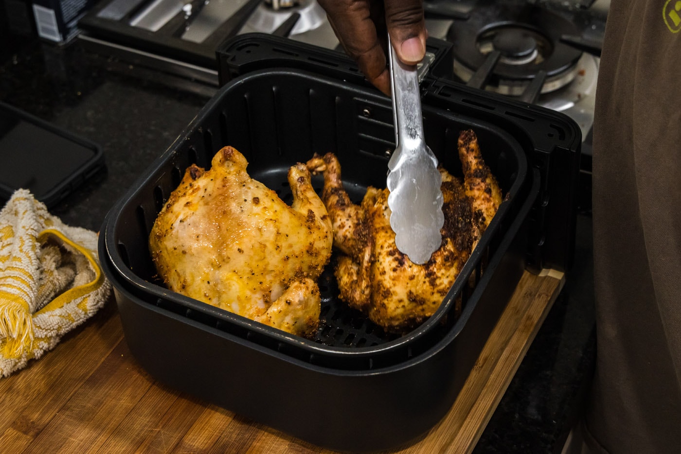 tongs flipping cornish hens over in an air fryer basket