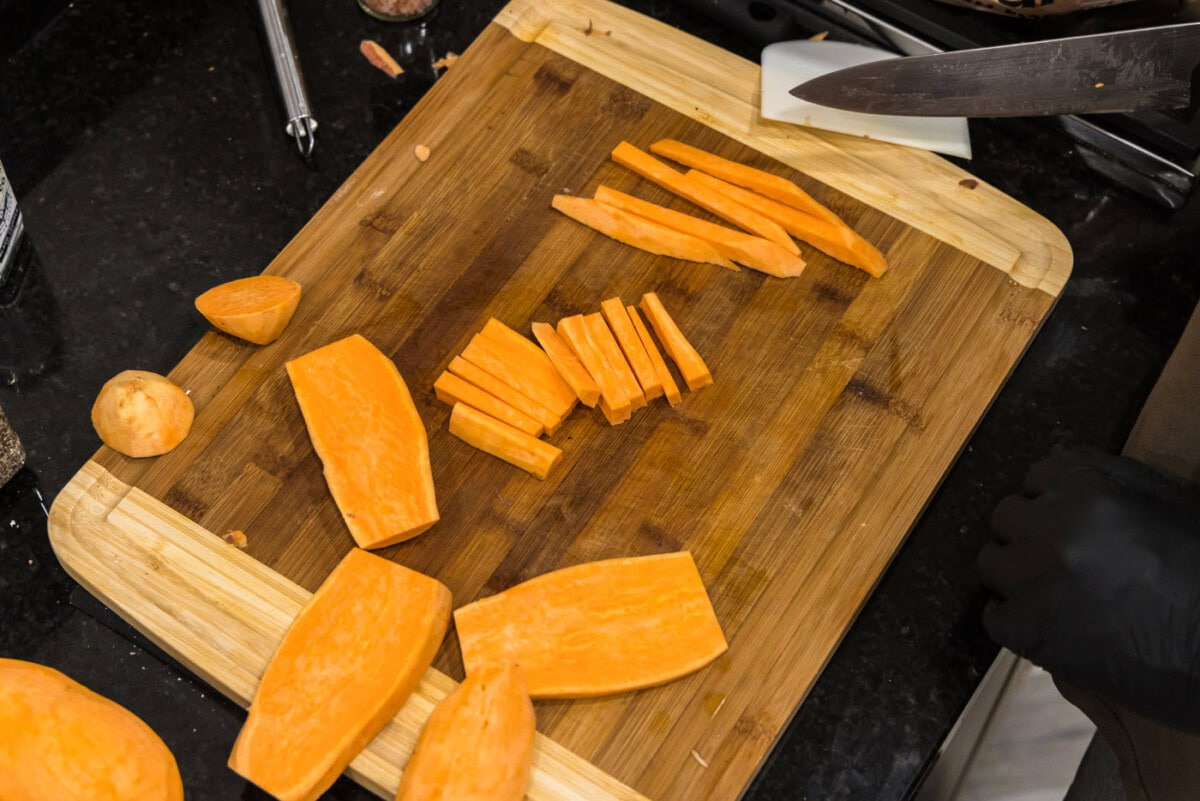 slicing peeled sweet potatoes into sticks