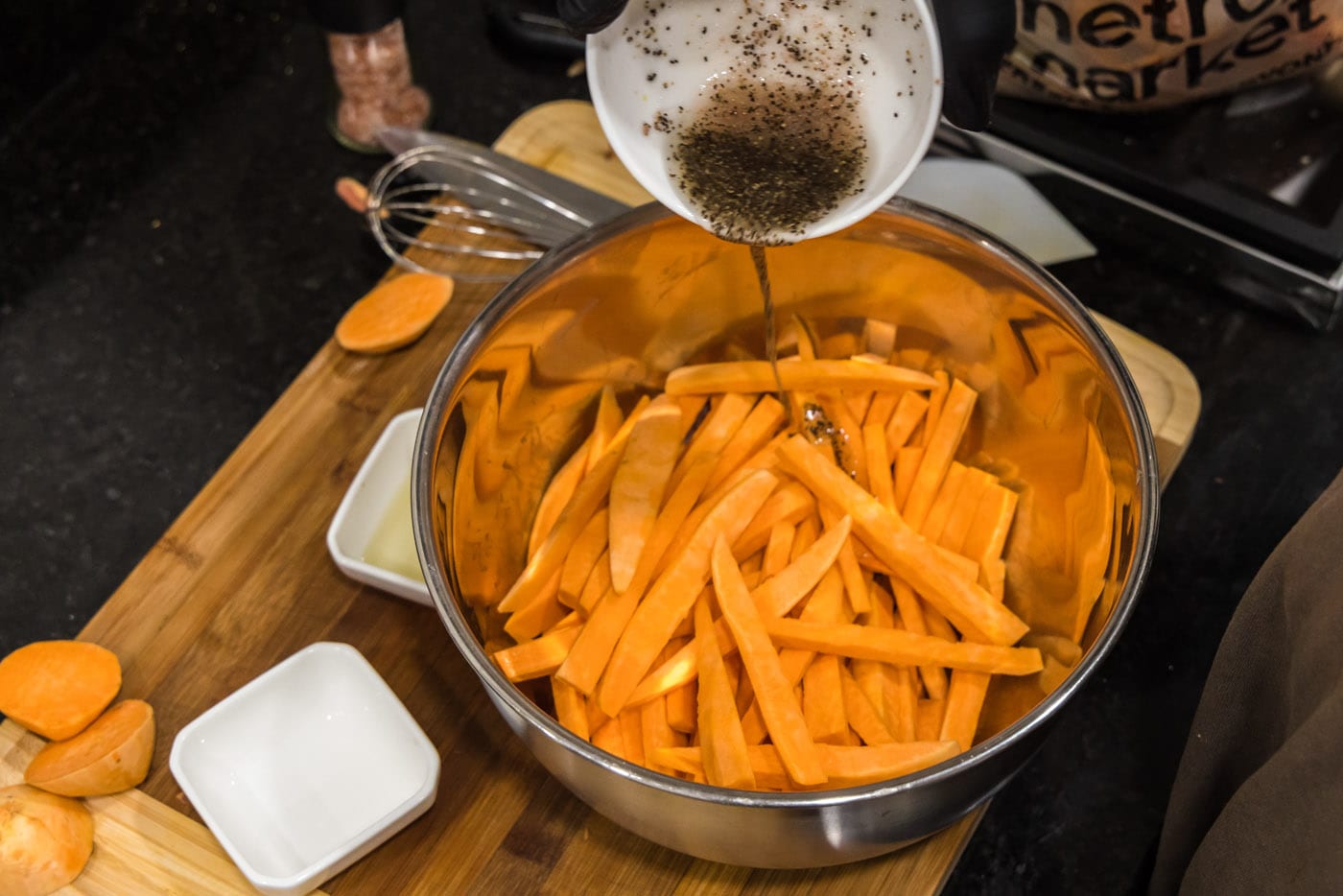 pouring olive oil, salt, and pepper over sweet potato fries