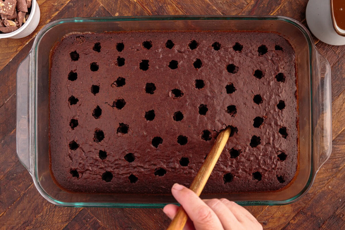 using a wooden spoon to poke holes into a cake