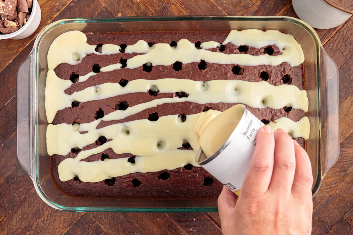 pouring sweetened condensed milk over poke cake