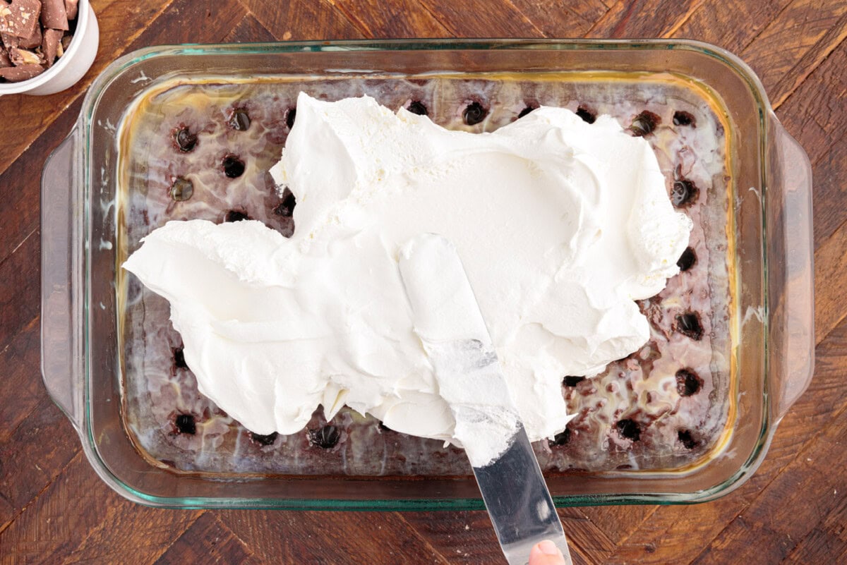spreading cool whip topping over poke cake