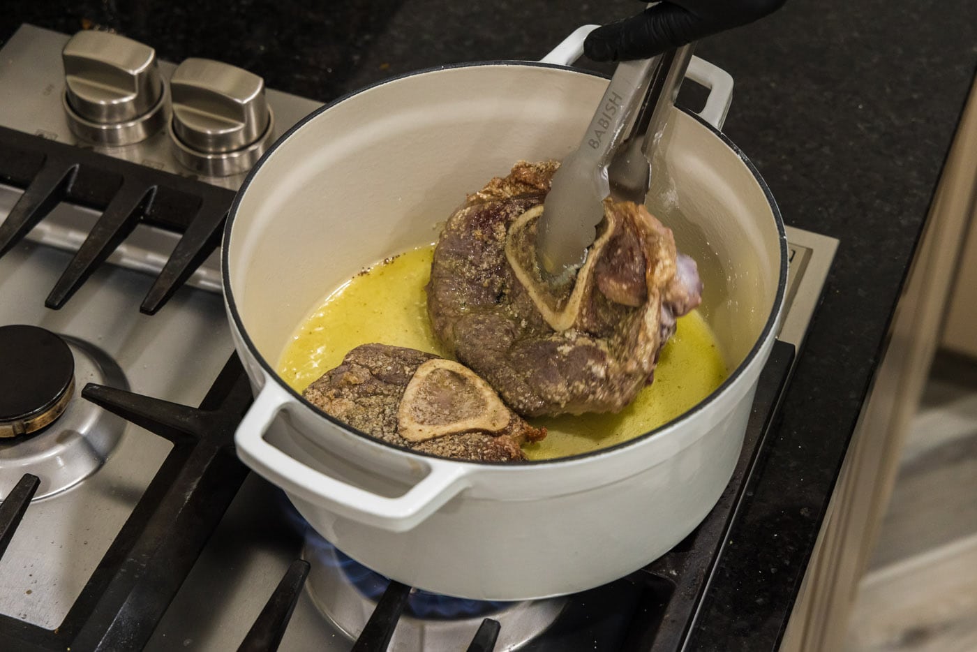 tongs flipping beef shanks in dutch oven