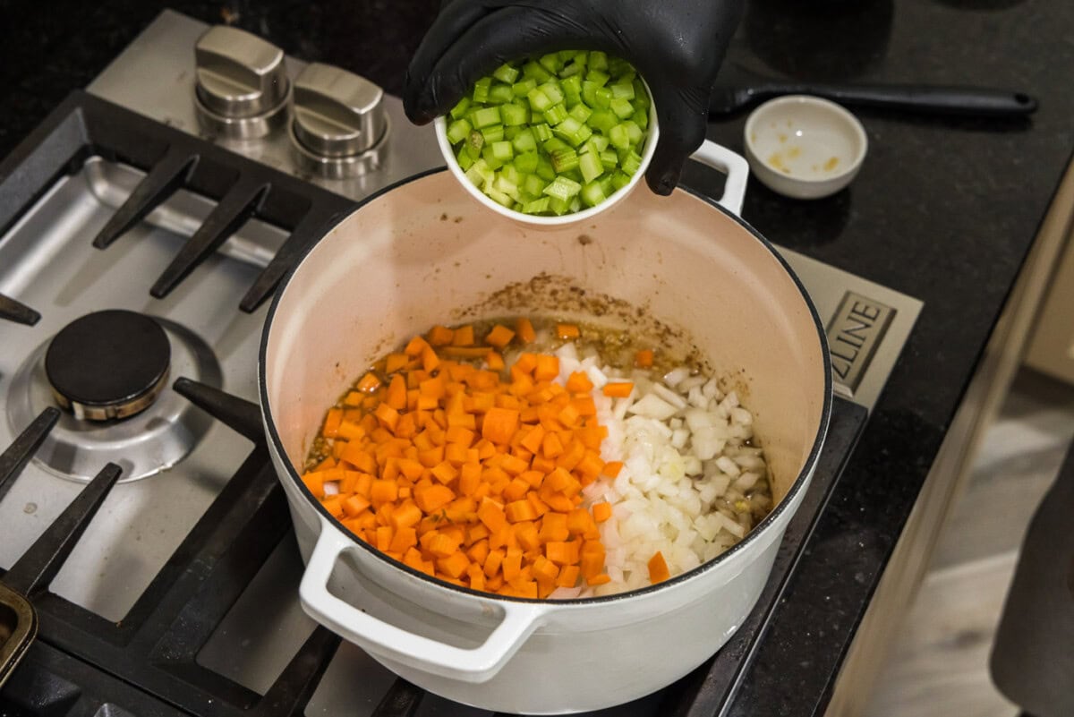 adding celery to pot with carrots, onion, and garlic in white wine