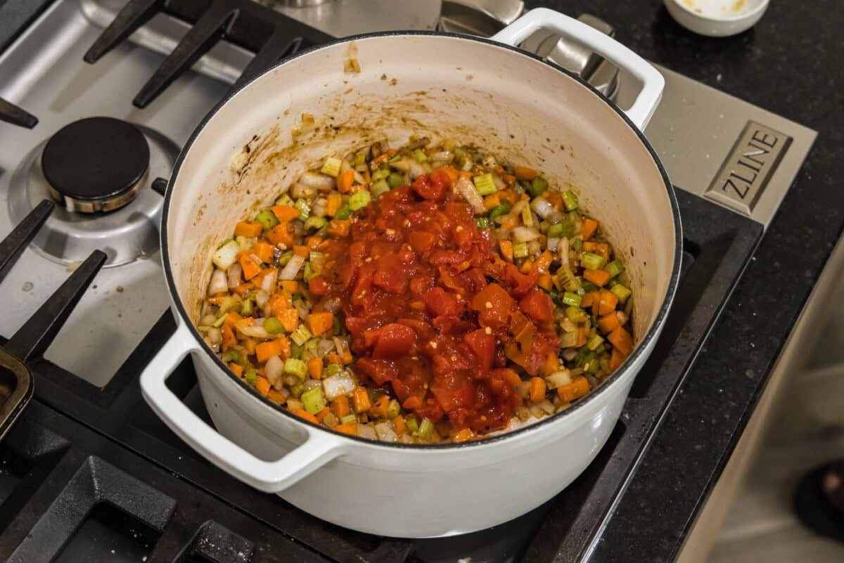 adding tomatoes to celery, onions, and carrots in pot