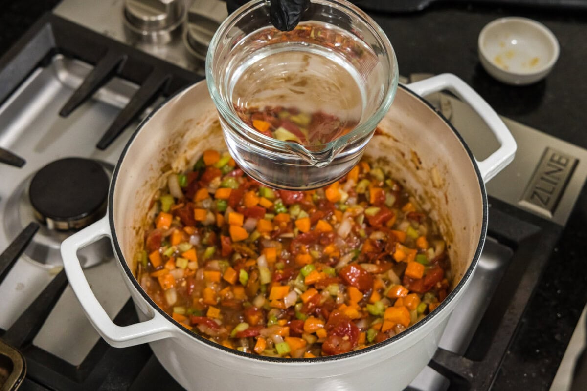 pouring water into dutch oven with vegetables