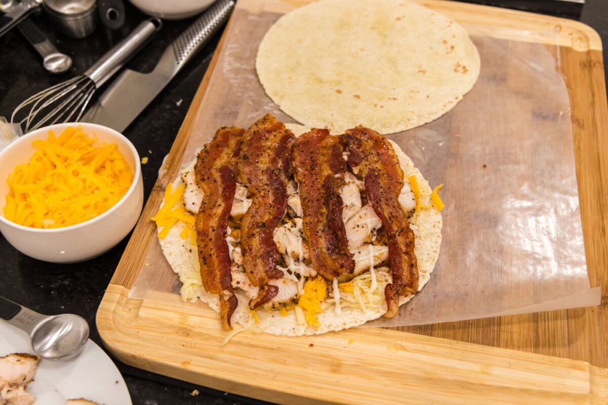 sliced bacon layered over ranch, chicken, and cheese tortilla