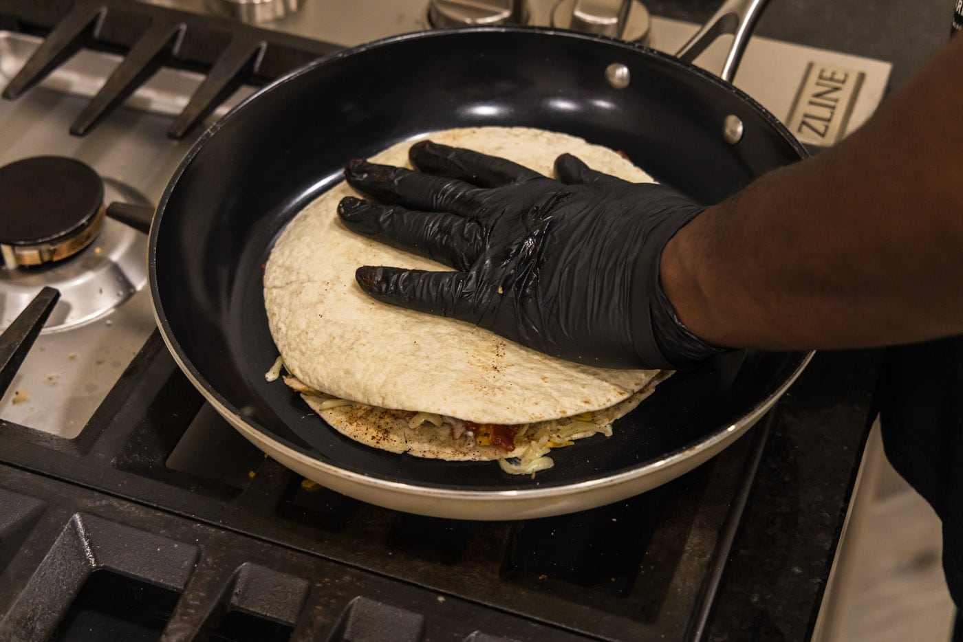 hand pressing down tortilla shell over the top of quesadilla in a skillet
