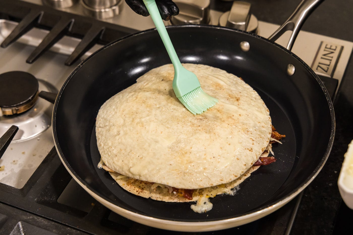basting tortilla shell with melted butter in a skillet