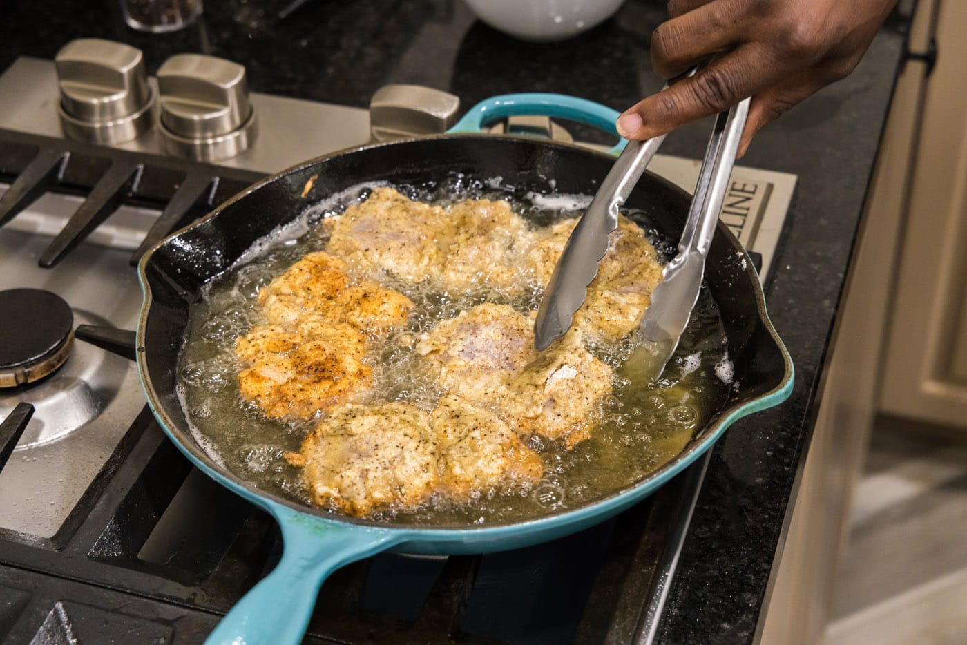 tongs flipping fried chicken in a skillet
