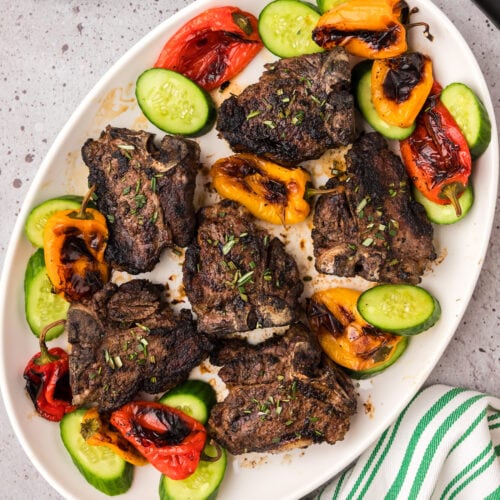 Grilled Lamb Loin Chops on a platter with roasted peppers and sliced cucumbers