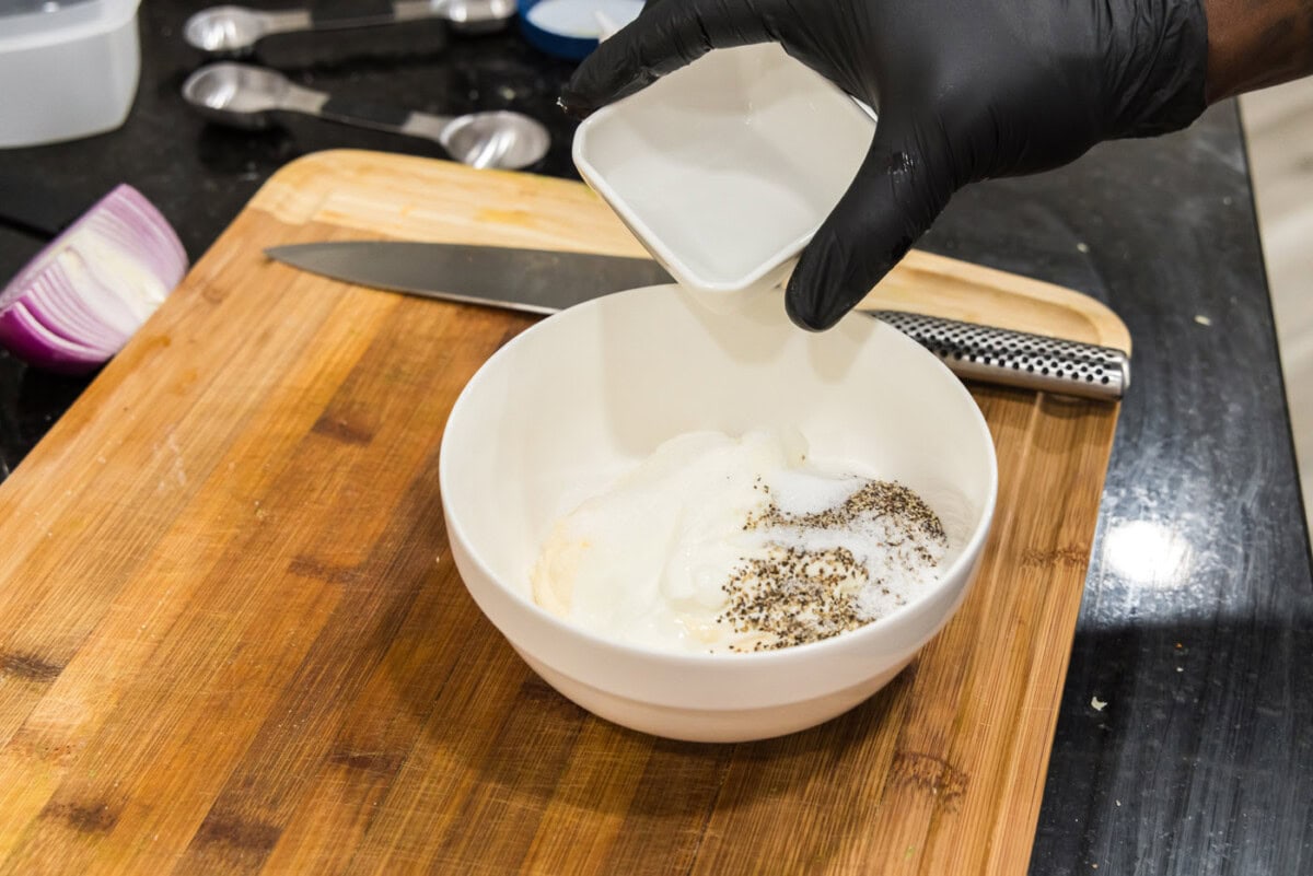 adding sugar to bowl with mayo, sour cream, and vinegar