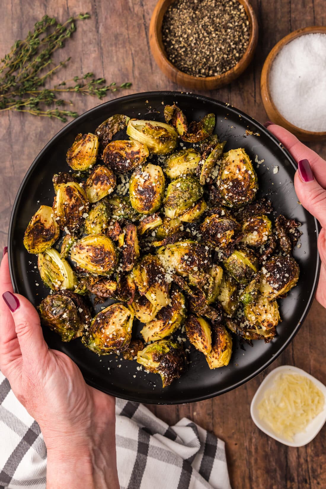 Hands holding a plate of Roasted Brussel Sprouts topped with parmesan