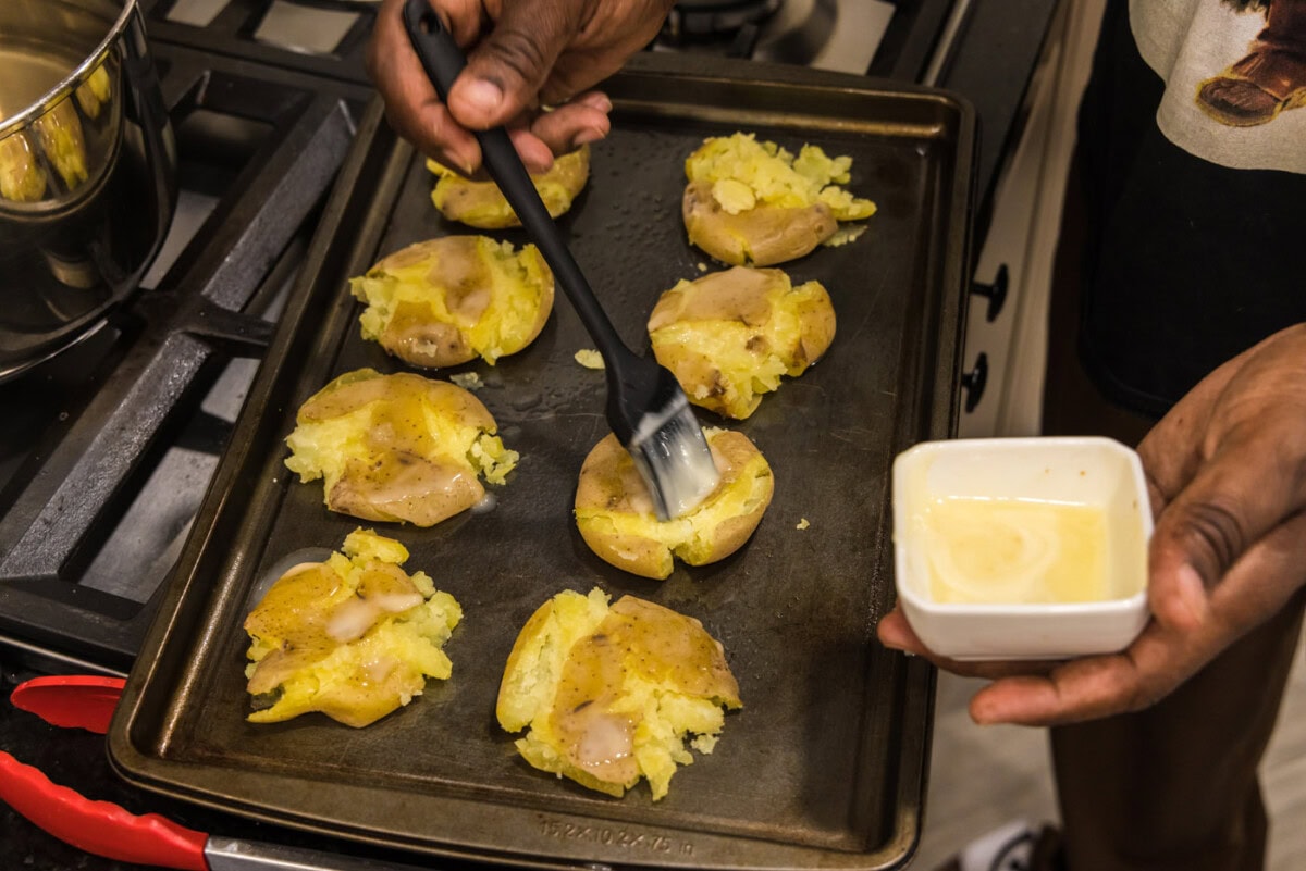 rubbing smashed potatoes with melted butter on a baking sheet