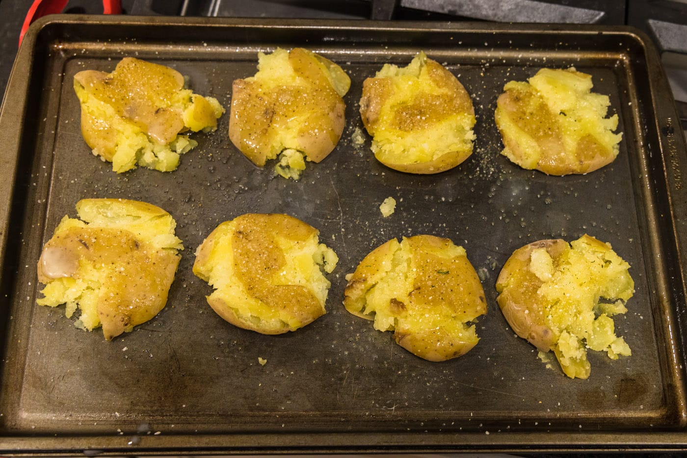 seasoned and butter basted smashed potatoes on a baking sheet