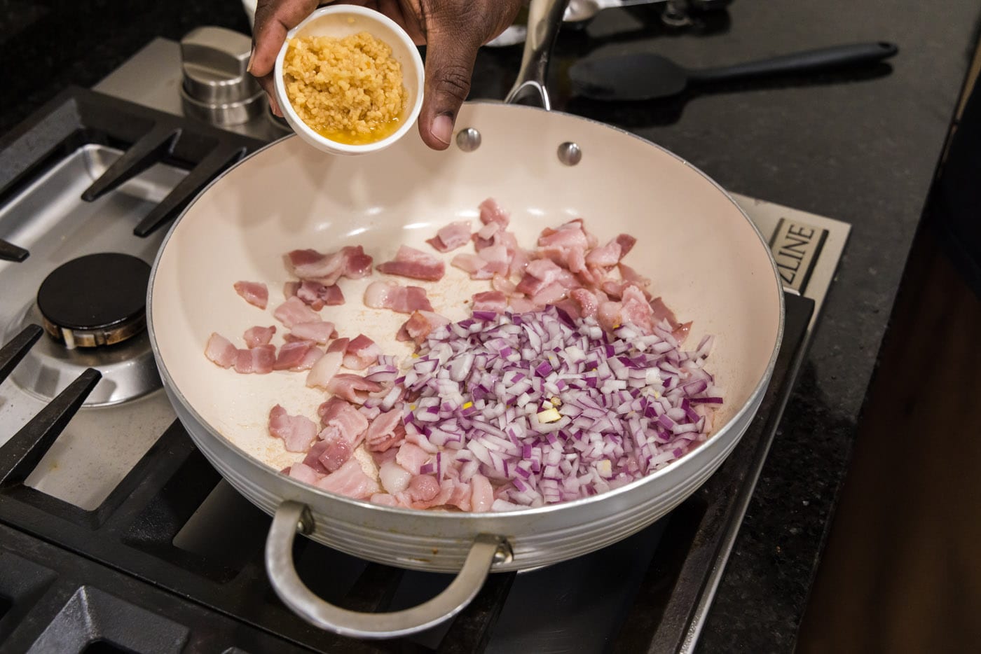 adding garlic to skillet with shallots and bacon