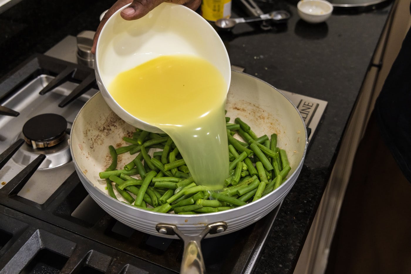 pouring chicken stock into skillet with green beans