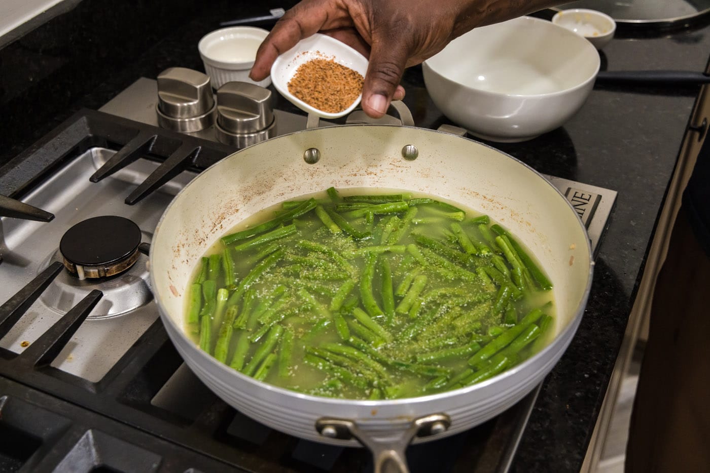 adding cajun seasoning to southern green beans in a skillet