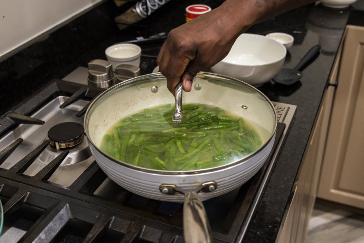 placing lid on skillet over green beans to cook