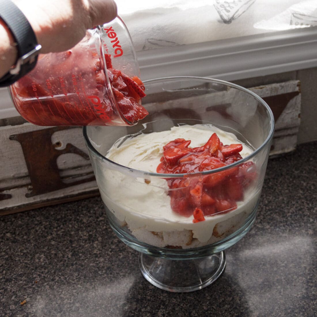 adding strawberry sauce over cream cheese layer in trifle bowl
