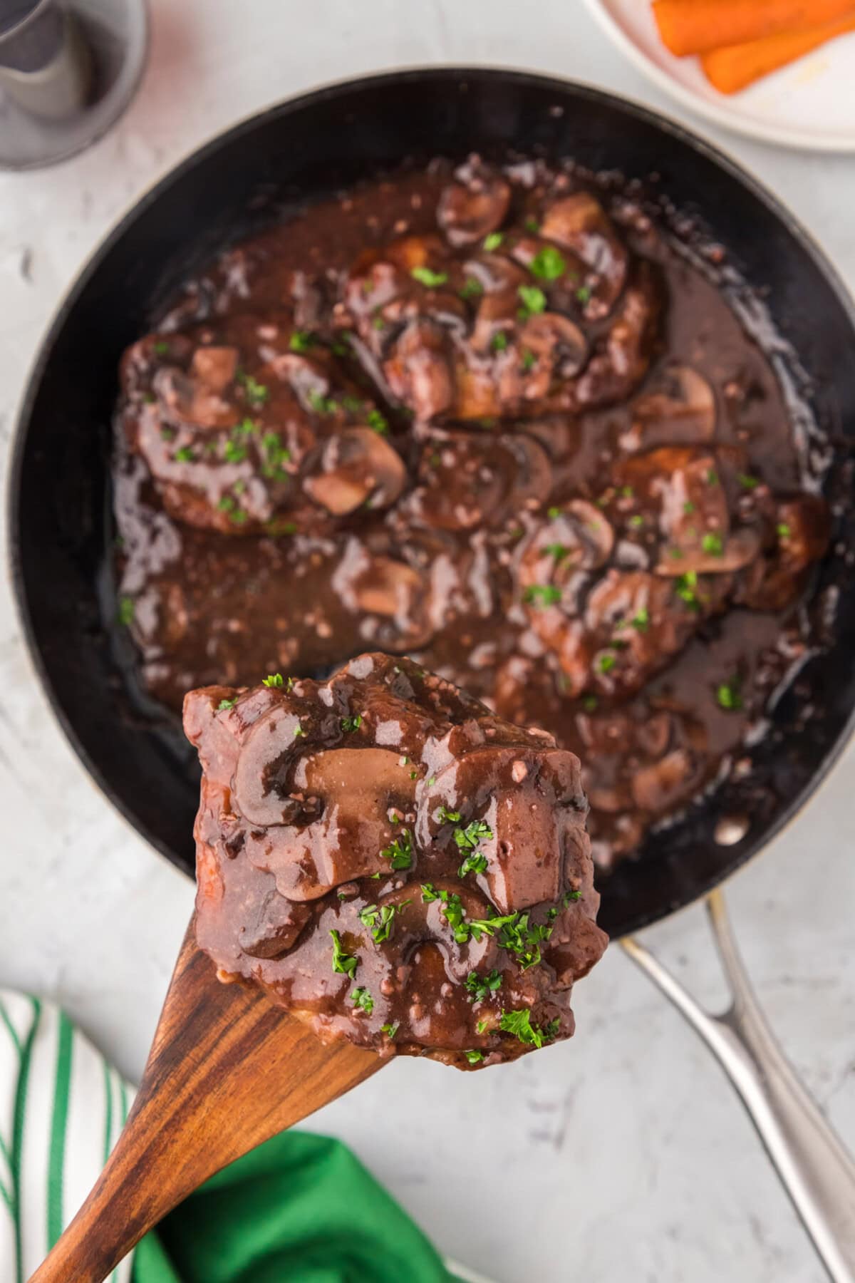 Wooden spatula lifting Veal Marsala out of a skillet of Veal Marsala
