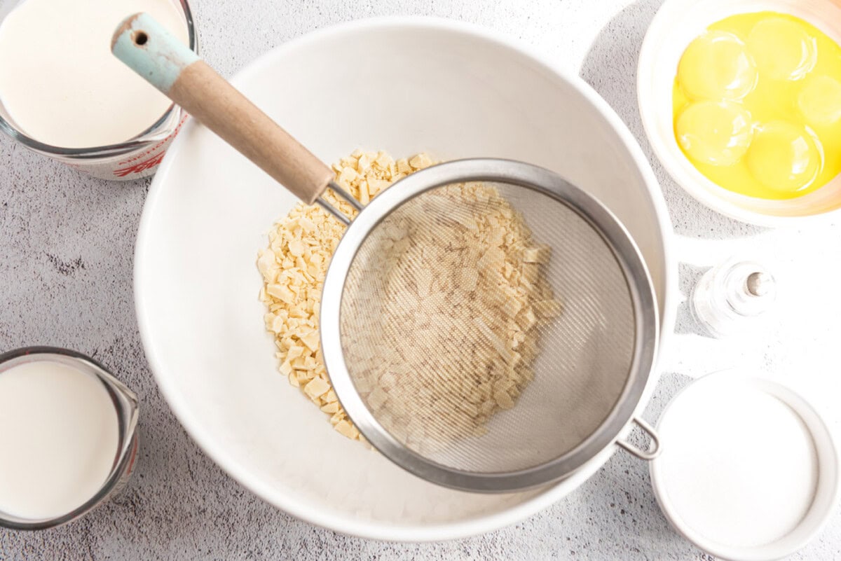 A photo of chopped white chocolate in a bowl and a mesh strainer over the top.