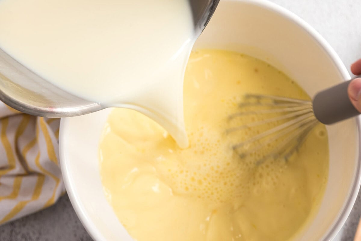 Milk mixture being poured into the whisked egg yolks