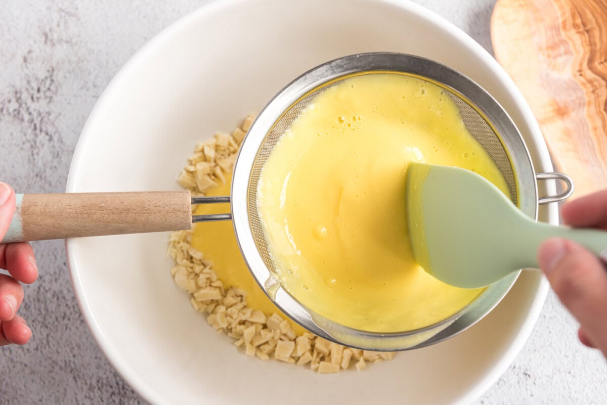 Custard` being strained over chopped white chocolate