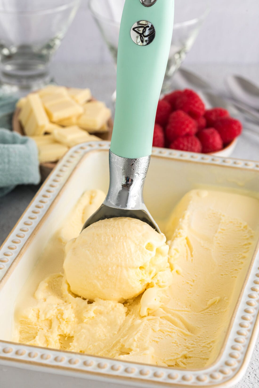 Ice cream scooper with a scoop of White Chocolate Ice Cream in a pan of White Chocolate Ice Cream