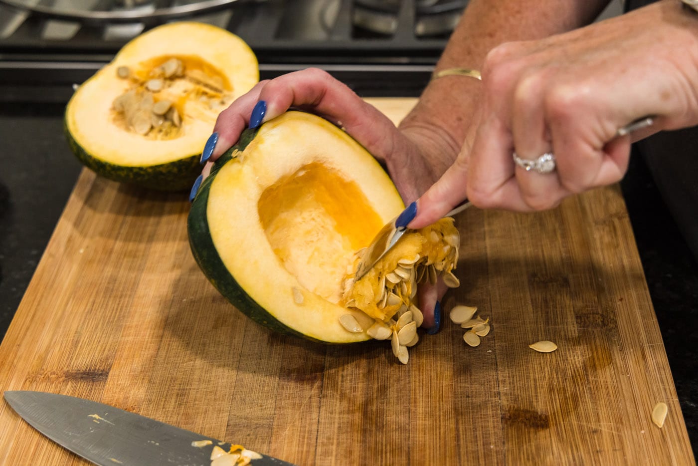 scooping the seeds out of an acorn squash with a spoon