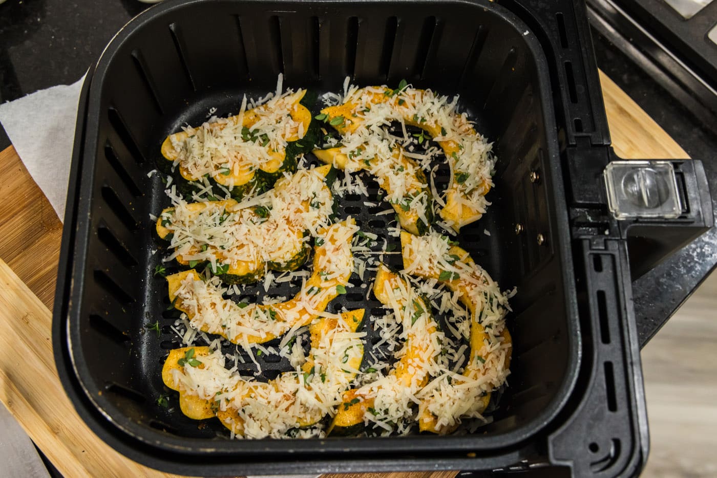 shredded parmesan cheese added to sliced acorn squash in an air fryer