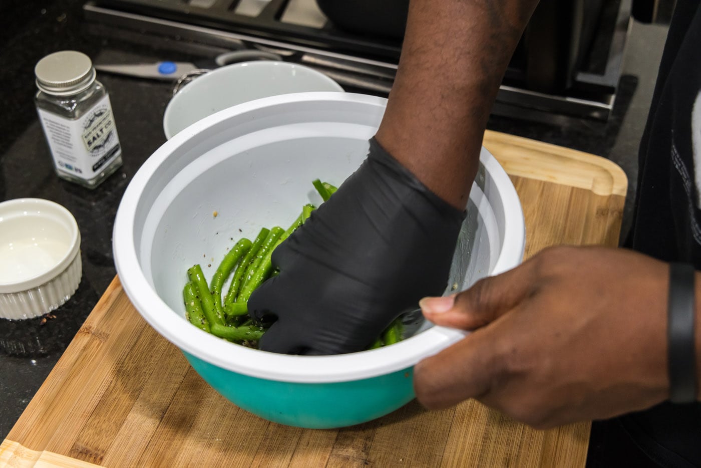 hand tossing green beans with seasonings in a bowl
