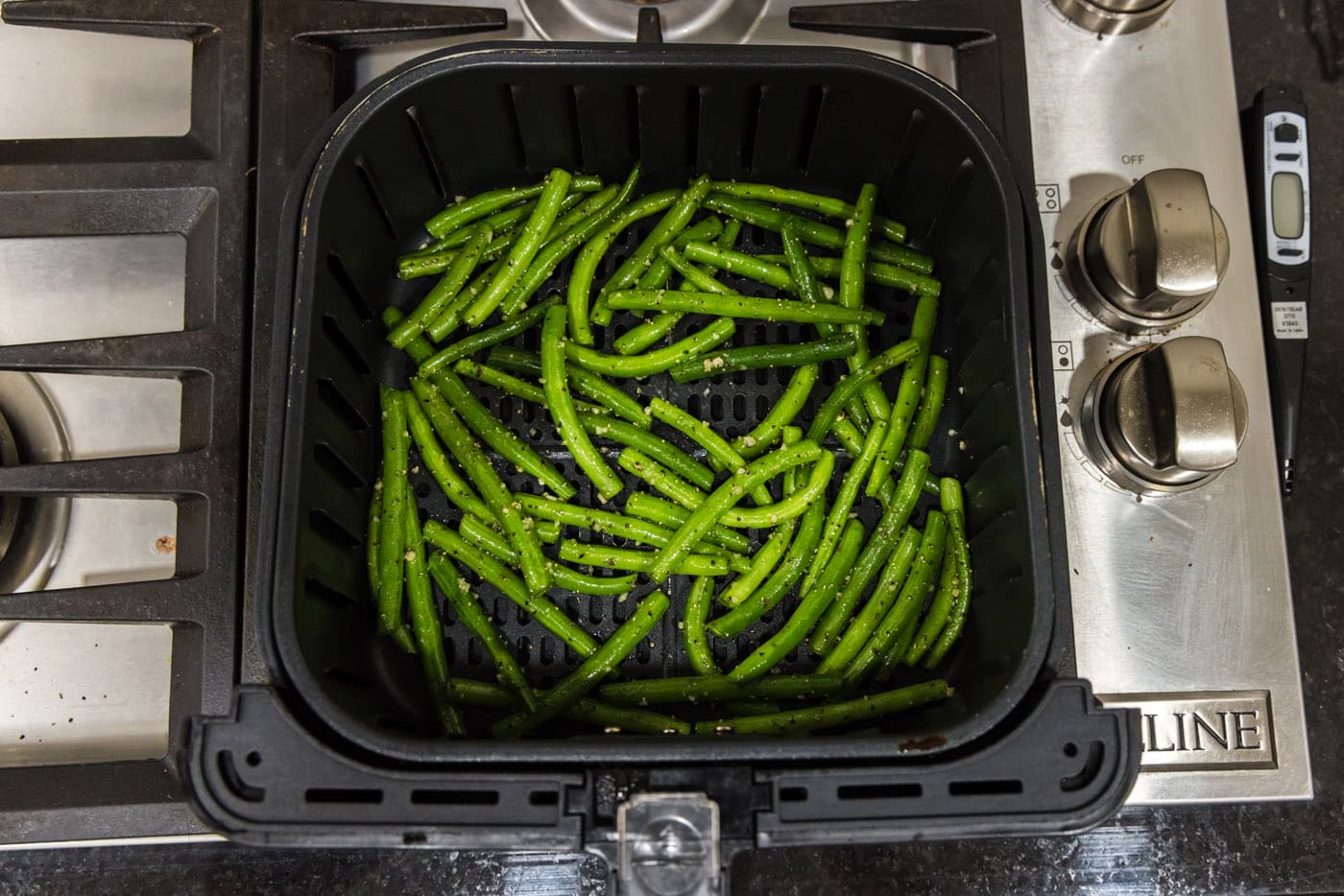 fresh green beans with seasoning and garlic in an air fryer basket