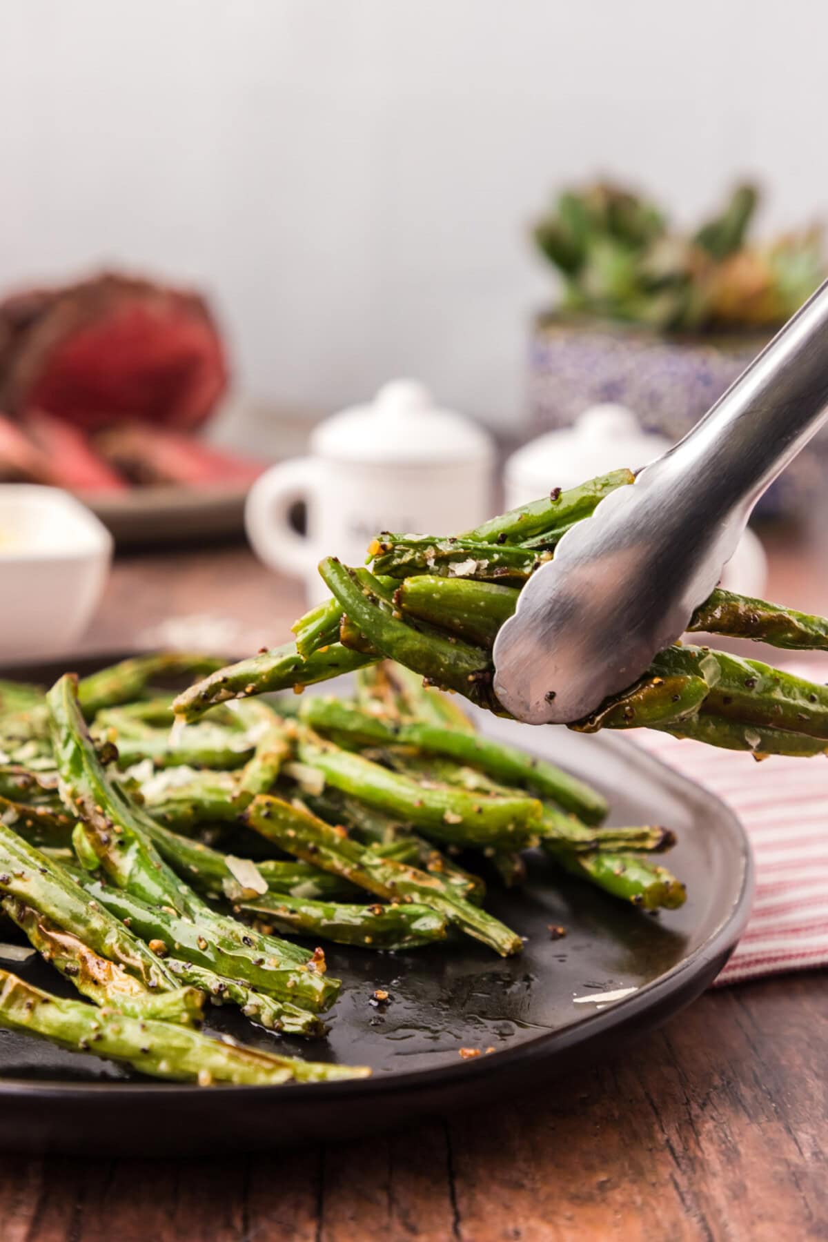 Tongs holding Air Fryer Green Beans above a plate of Air Fryer Green Beans