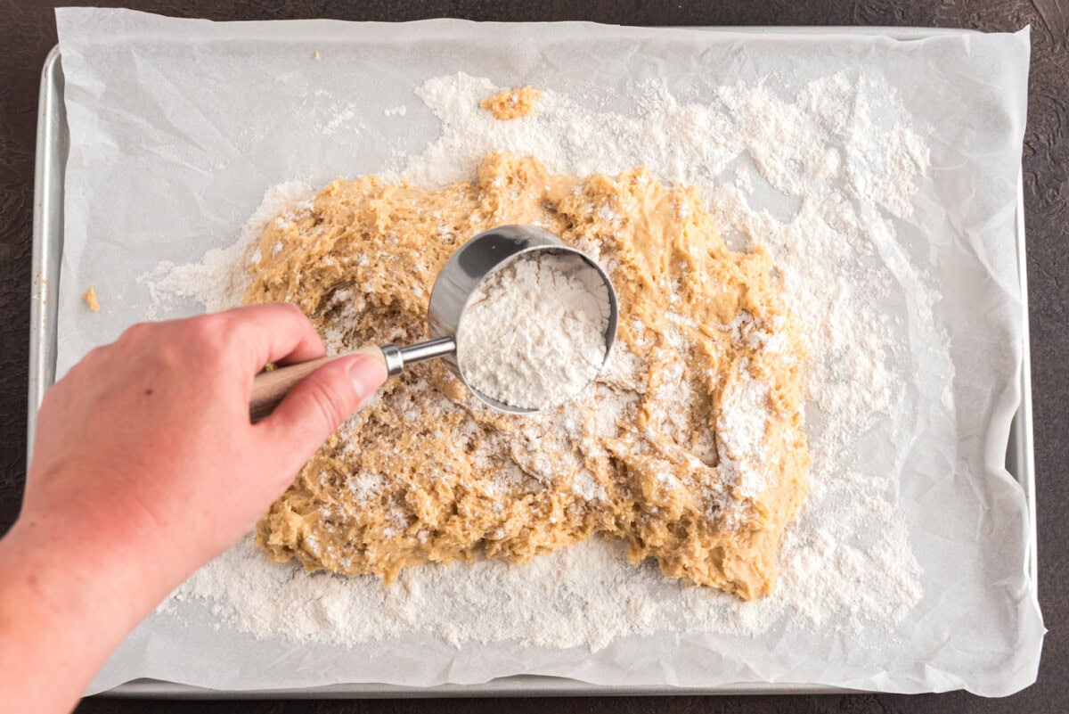 adding flour over doughnut dough on parchment paper