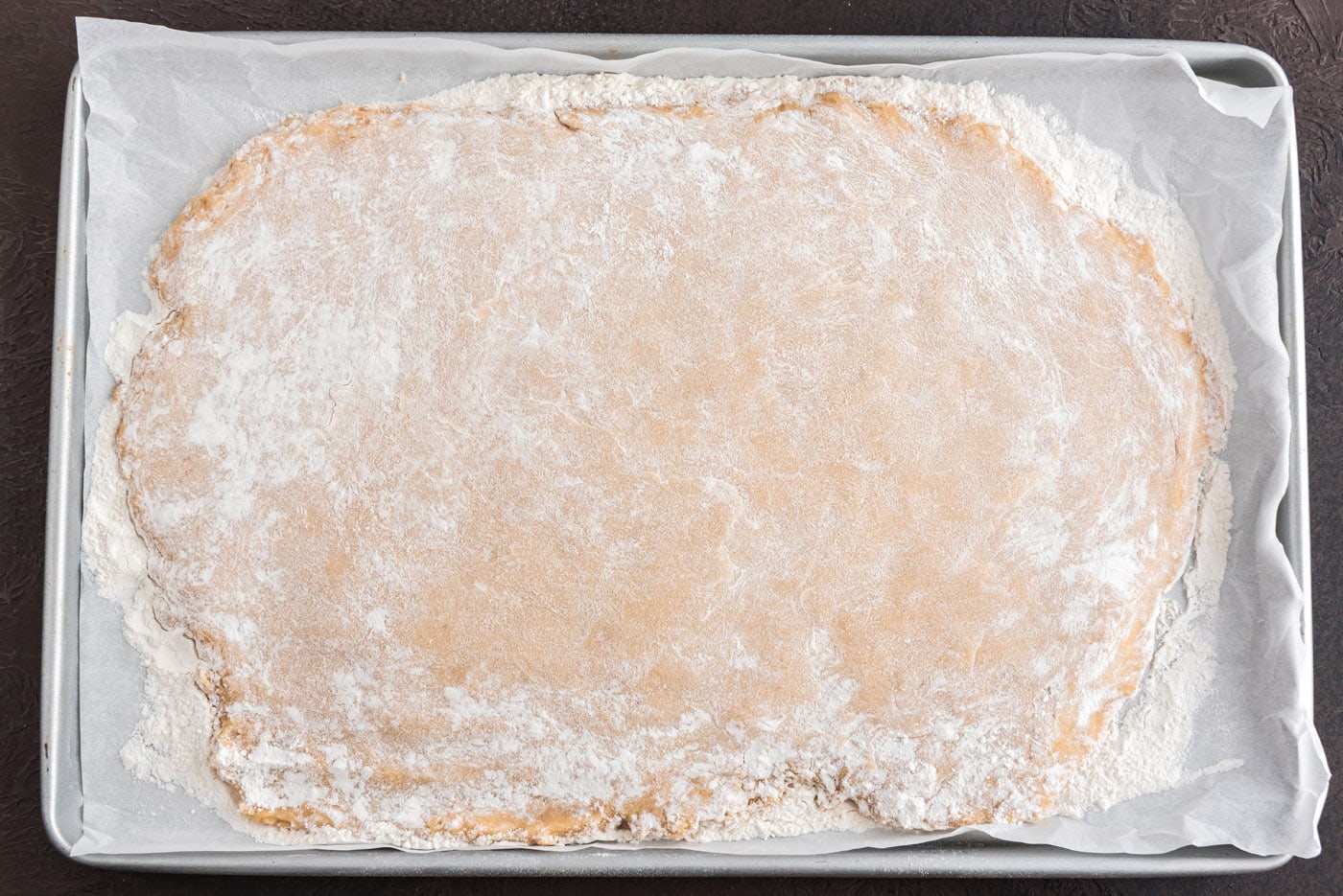flattened donut dough on a baking sheet