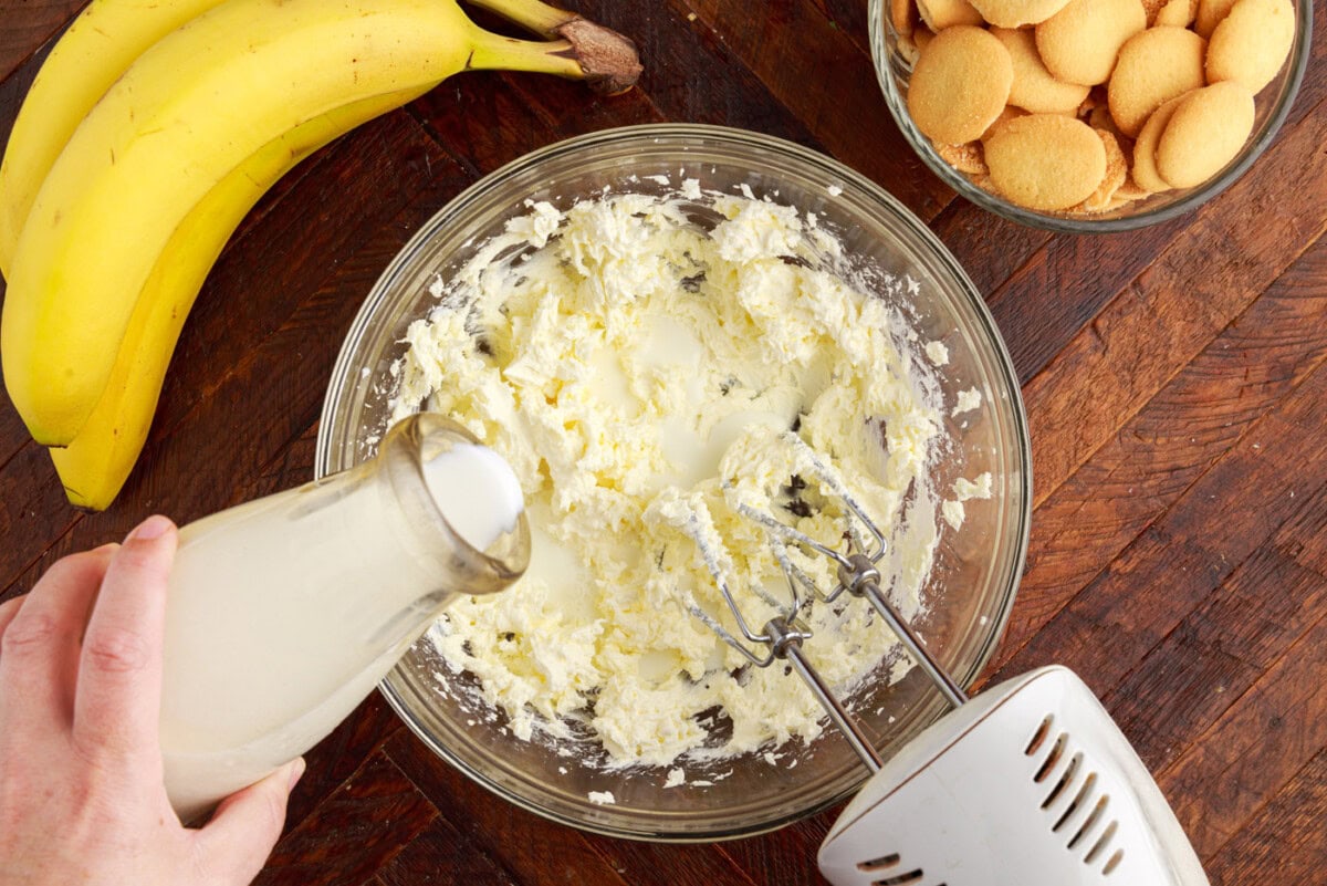 adding whole milk to whipped cream cheese in a bowl with a mixer