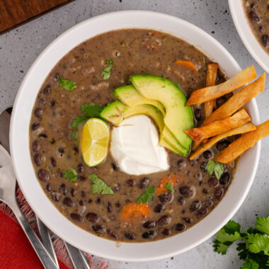 Bowl of Black Bean Soup topped with lime, sour cream, avocado and tortilla strips