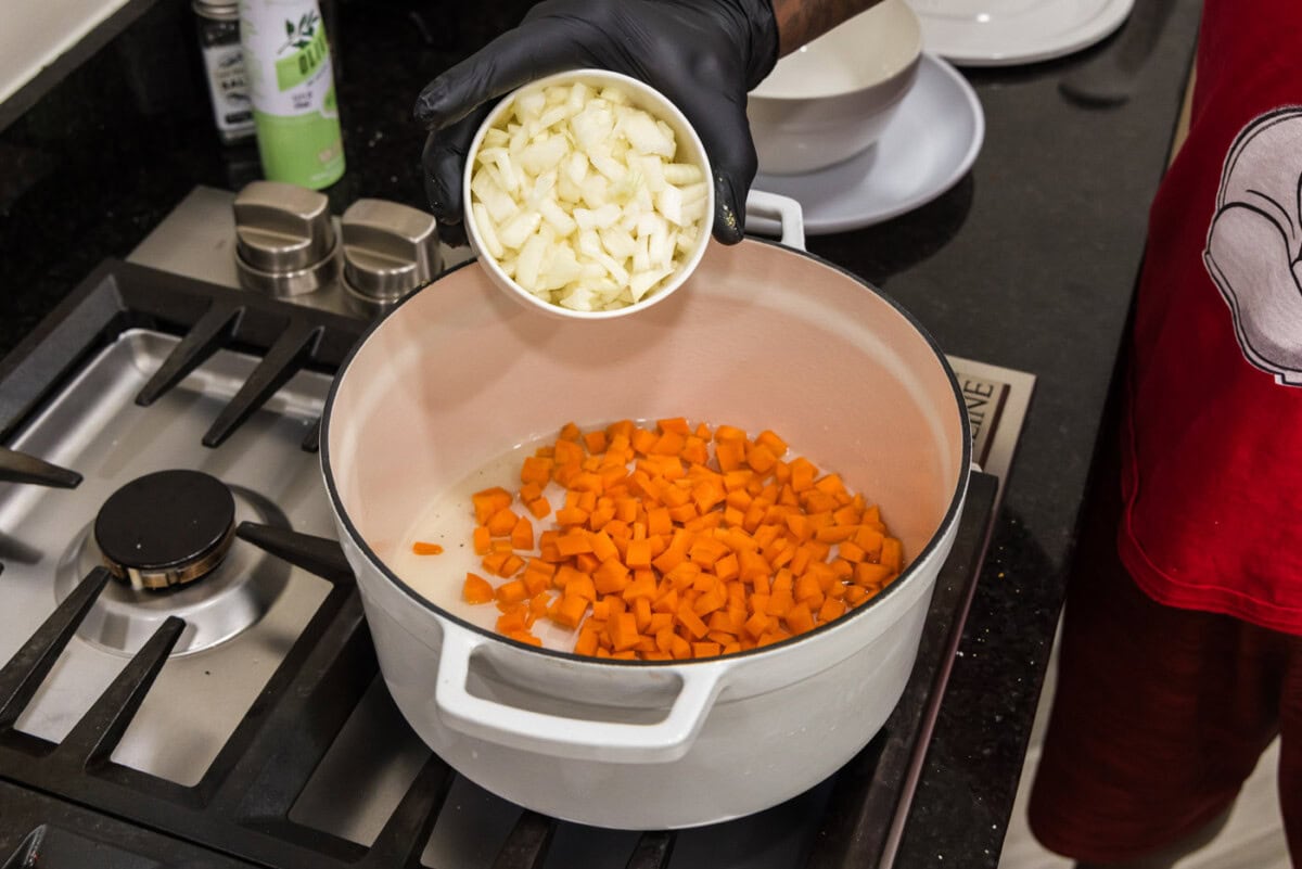 pouring onion into dutch oven with carrots