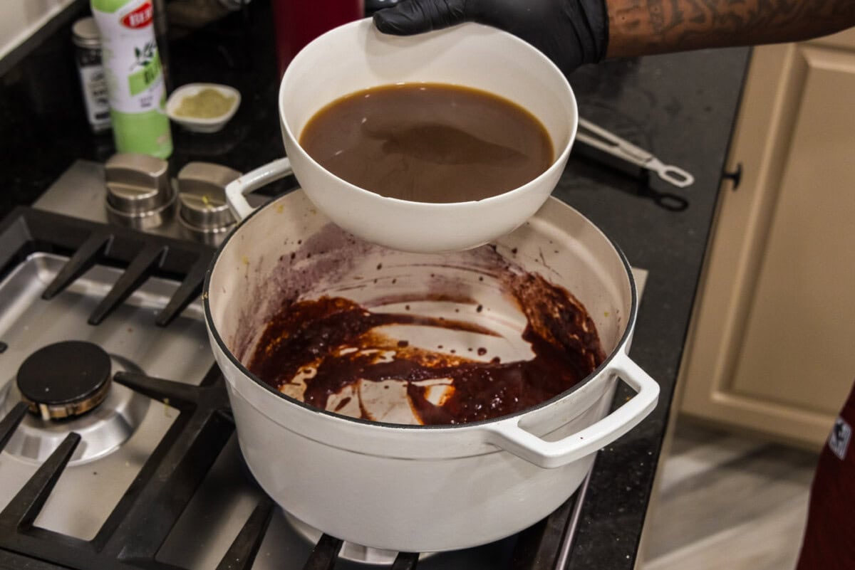 pouring beef broth into red wine and tomato paste mixture