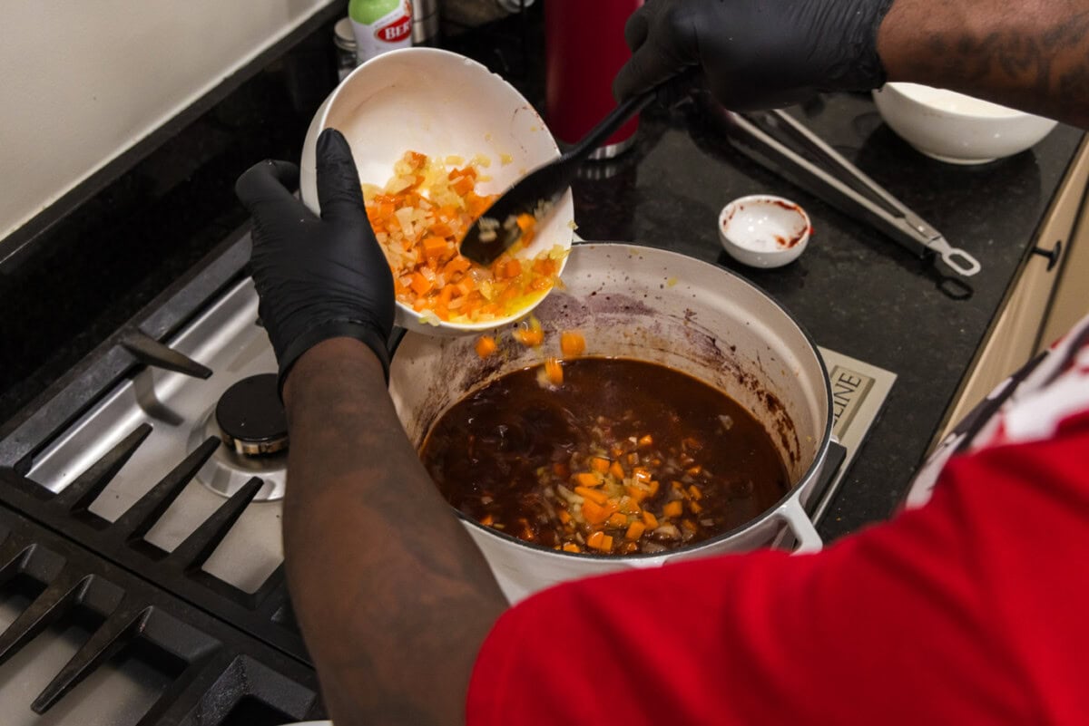 adding sauteed carrots and onions to pot with red wine sauce