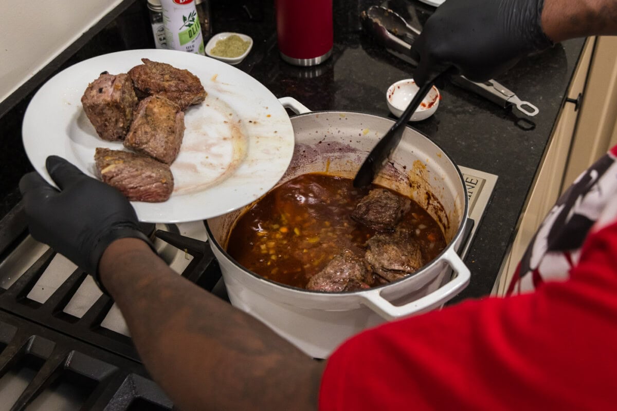 adding short ribs to pot with red wine sauce and vegetables