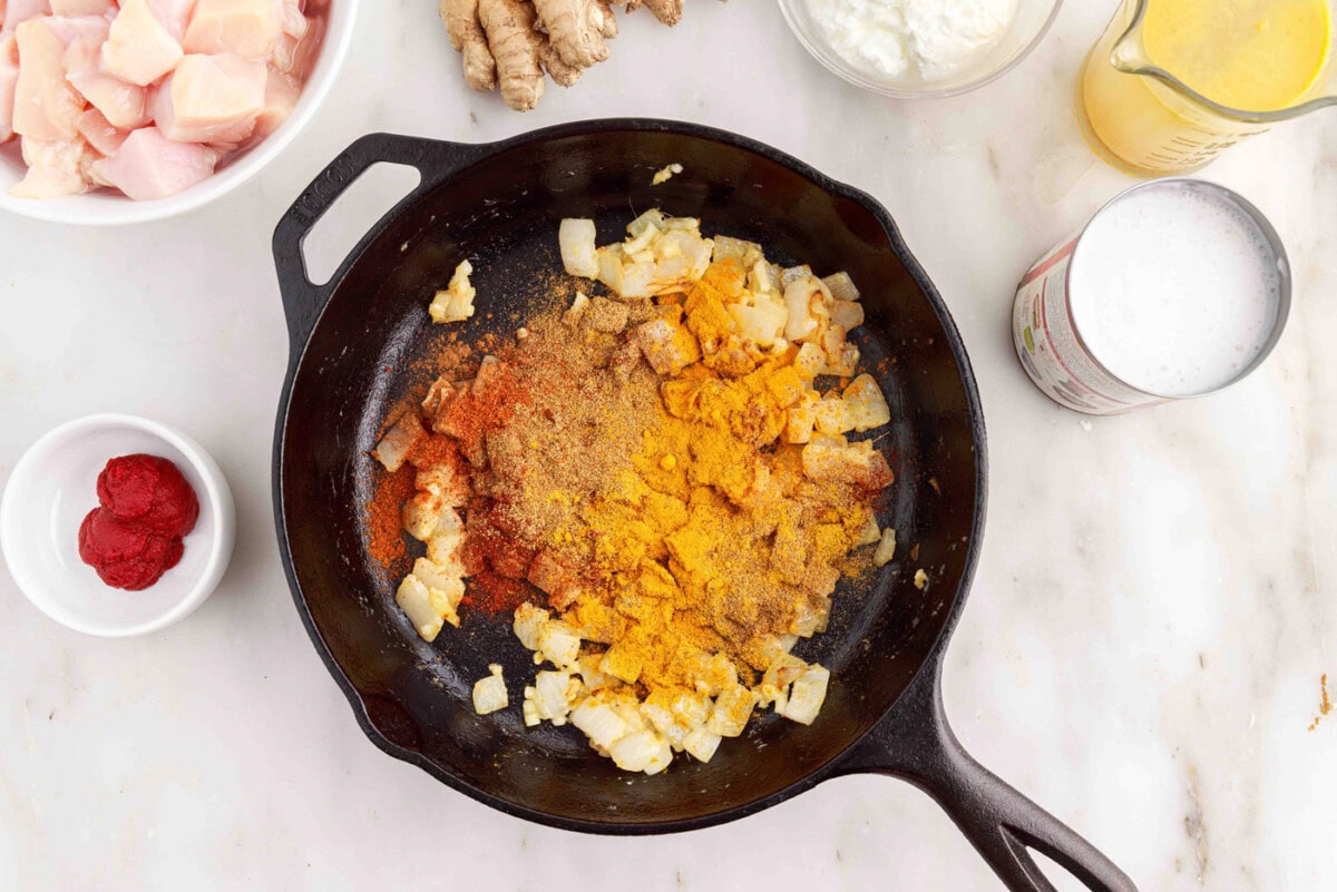 adding curry spices to skillet with onion, ginger, and garlic