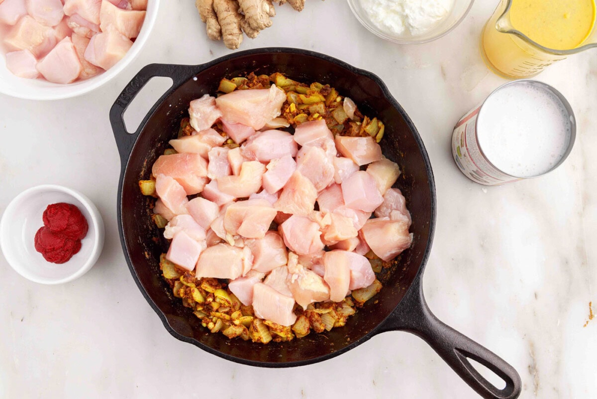cooking cubed chicken in a skillet with curry spices