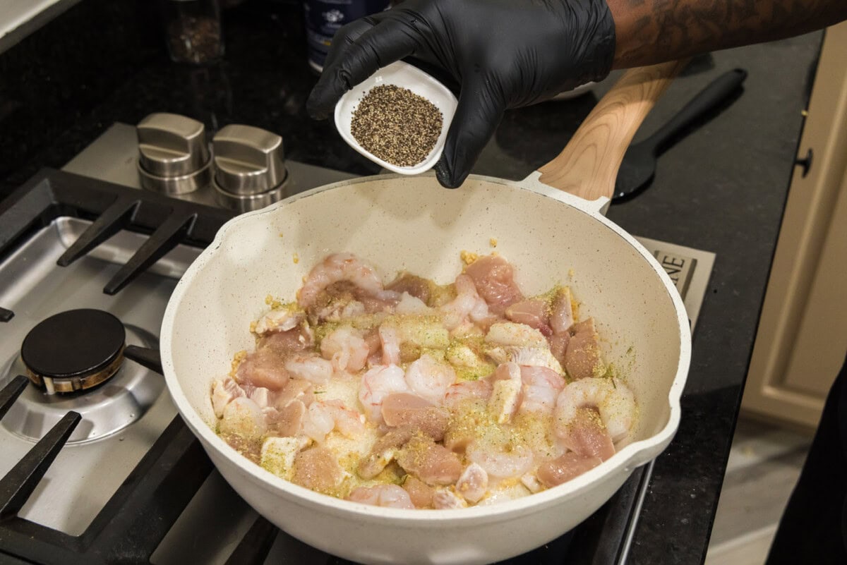 adding seasoning to skillet of shrimp, chicken, and garlic.
