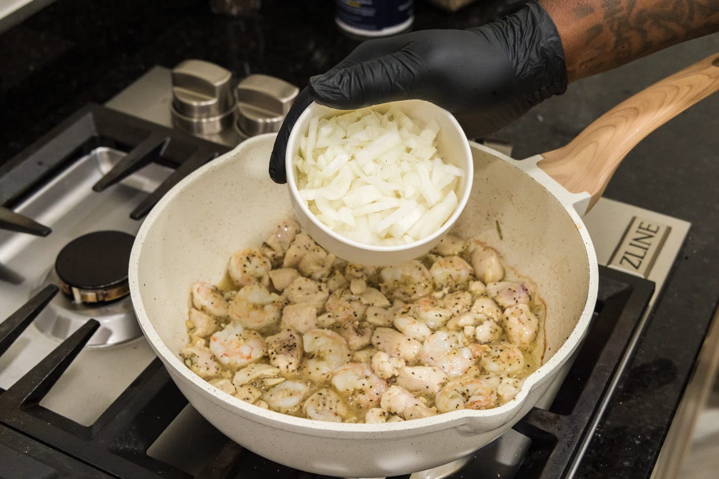Hand adding chopped onion to skillet with chicken and shrimp mixture