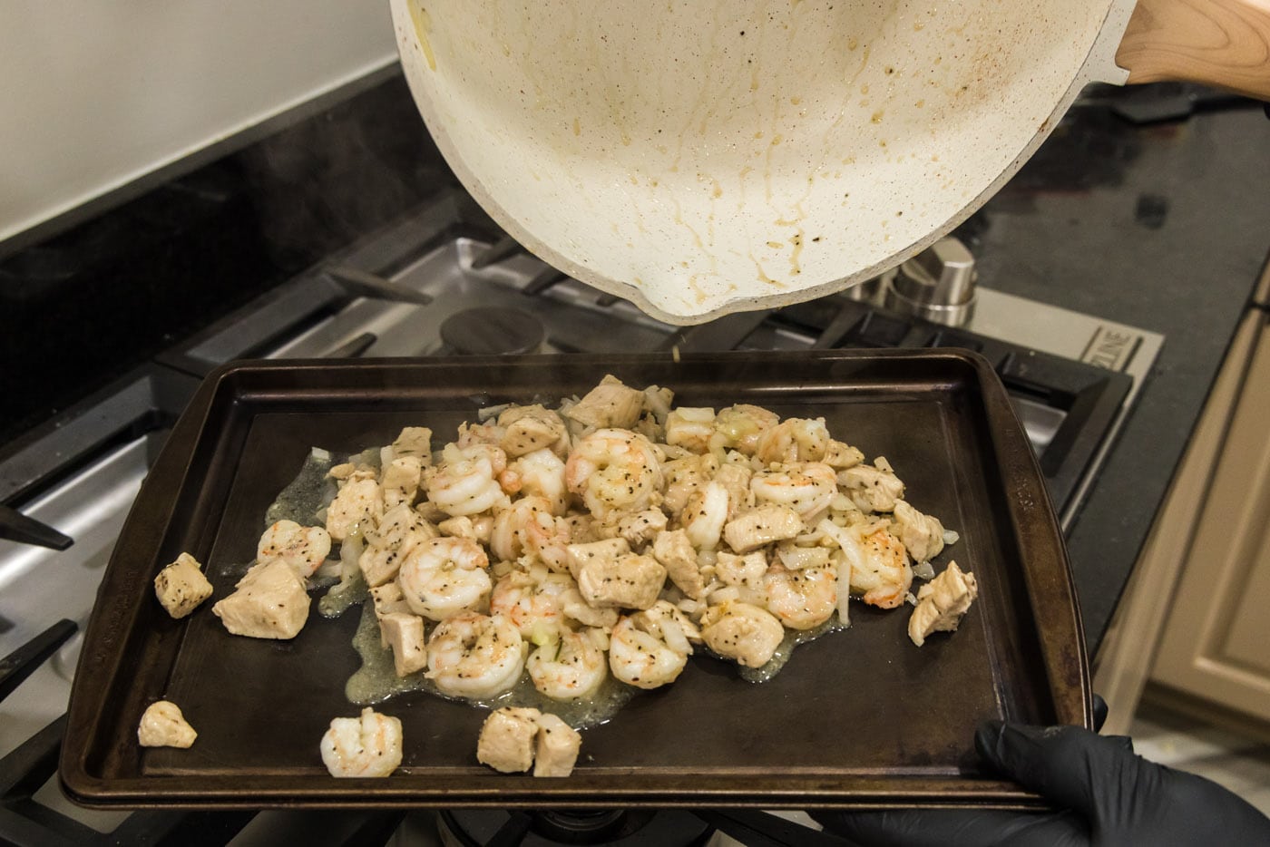 pouring chicken and shrimp mixture onto a baking sheet