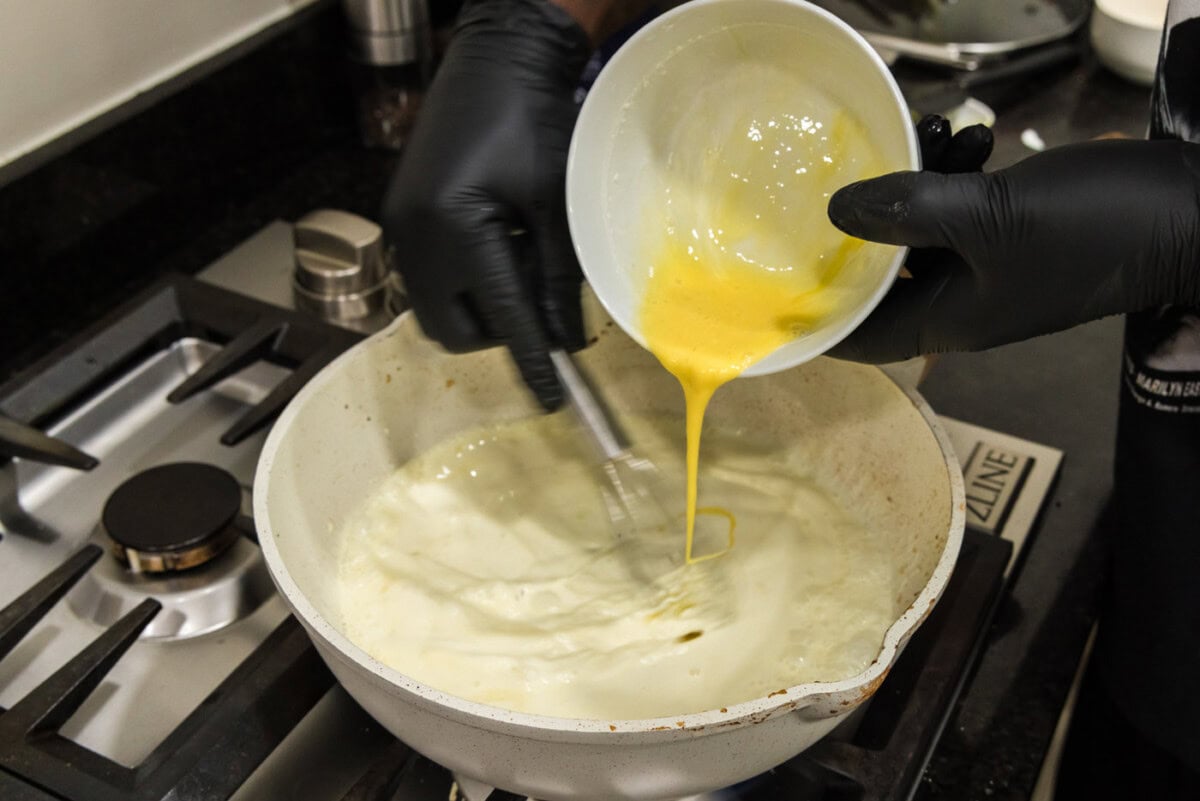 pouring whisked eggs into skillet of heavy cream while constantly whisking to combined