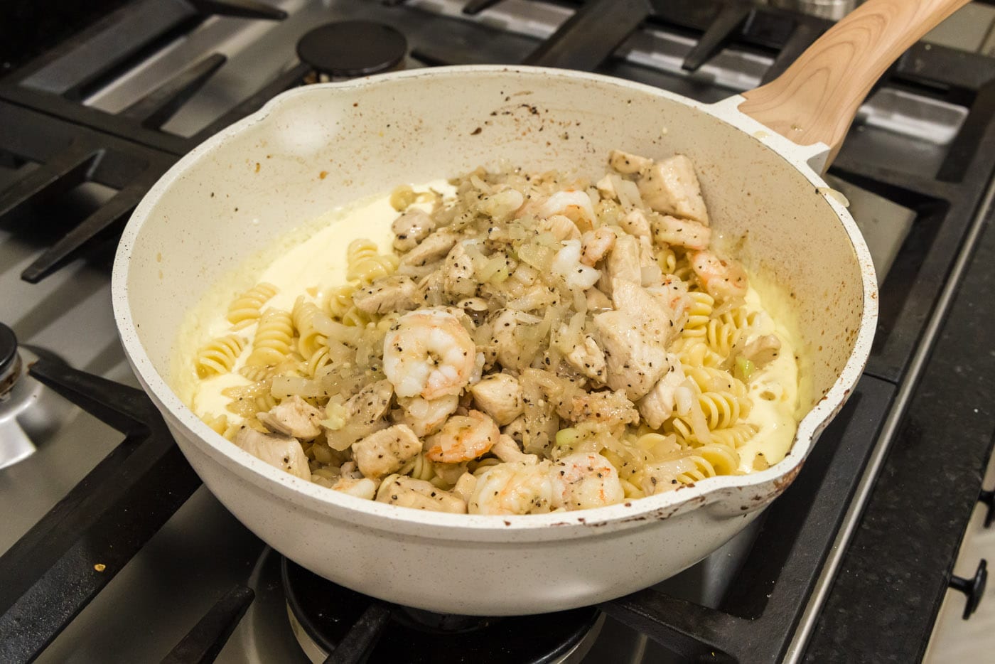adding chicken and shrimp mixture to skillet with pasta and carbonara sauce